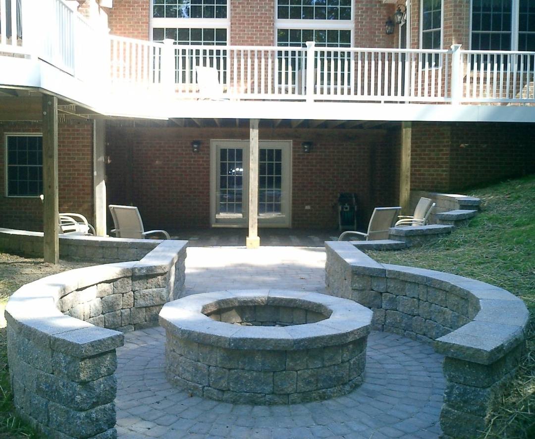 Round fire pit and curved seat walls on a paver patio below a deck