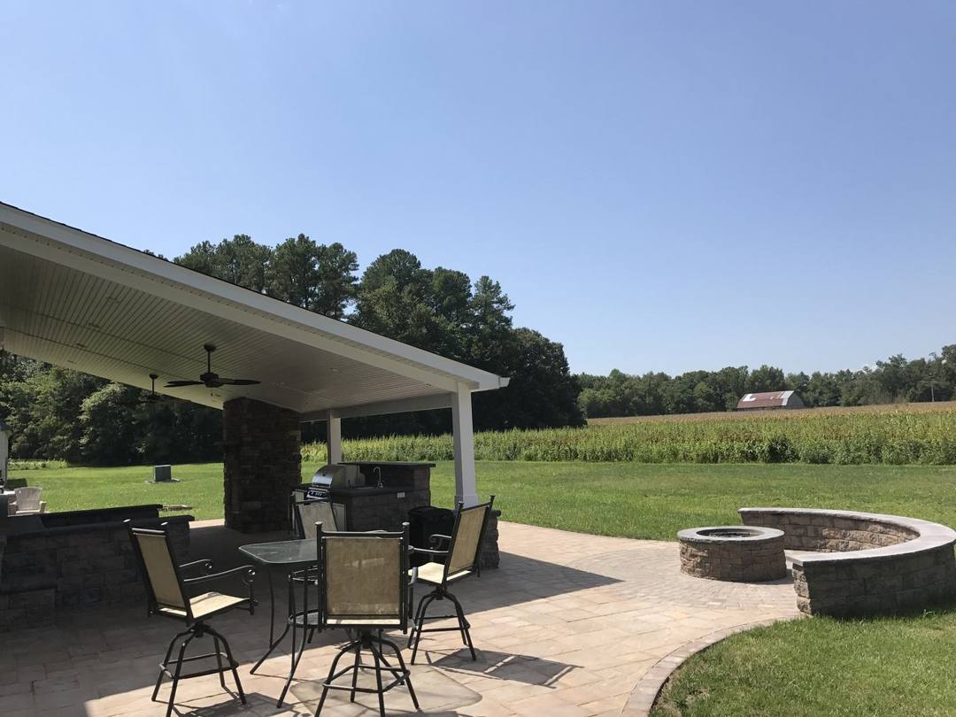 Covered patio with seating and a fire pit overlooking a field