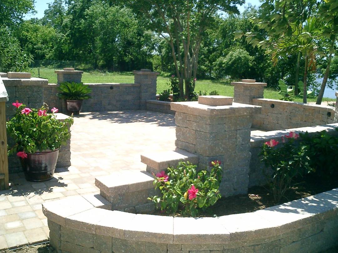 Paver patio with a curved seat wall, pillars, and flower planters