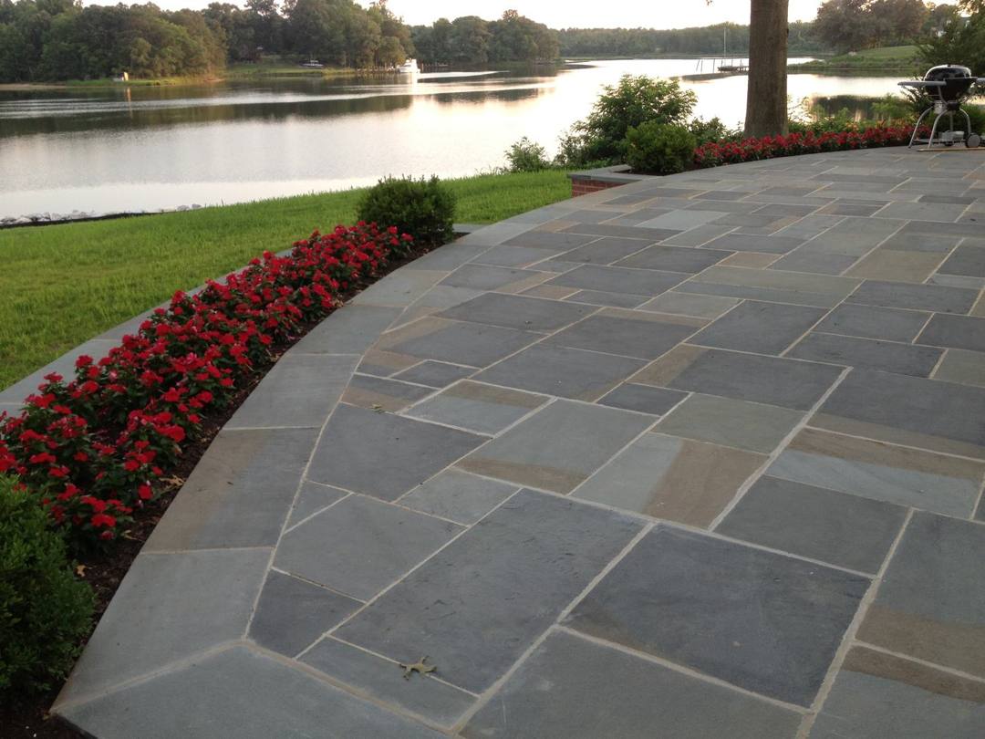 Curving flagstone patio bordered by red flowers along the water