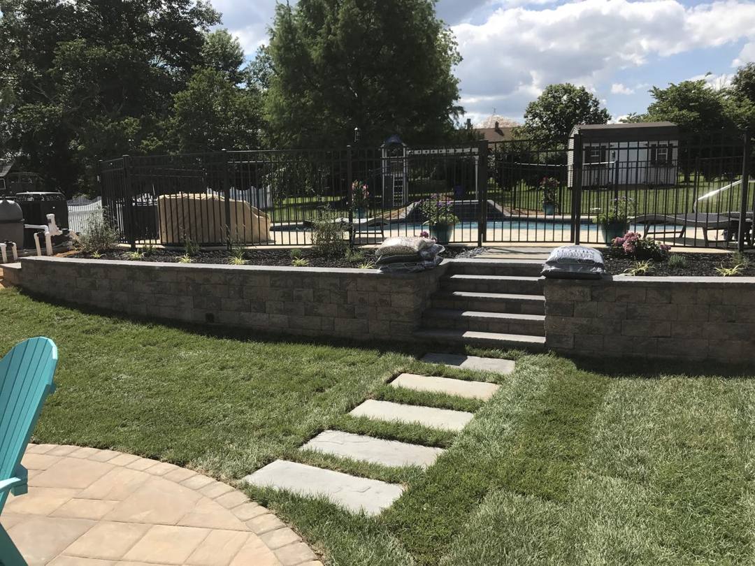 Low retaining walls and steps leading to a fenced pool, with stepping stones