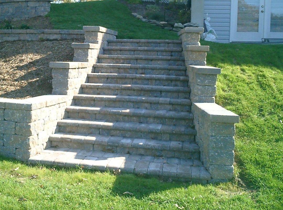 Wide paver steps with block pillars up a grassy slope
