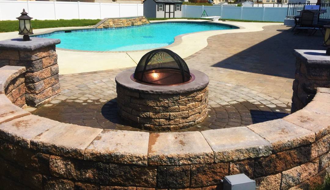 Stone fire pit and seat wall beside a pool in La Plata, MD