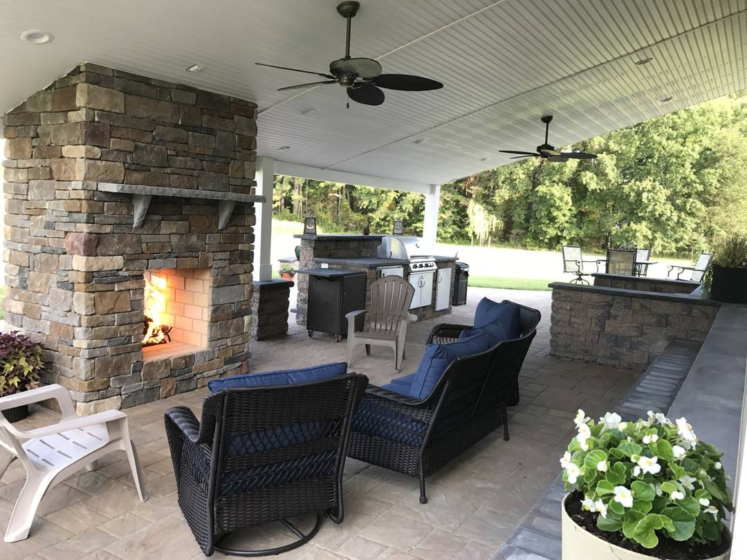 Stone outdoor fireplace and lounge seating with an outdoor kitchen on a covered patio