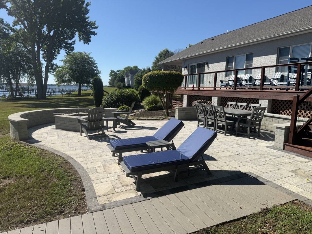 Waterfront paver patio with lounge chairs, a curved seat wall, and a fire pit