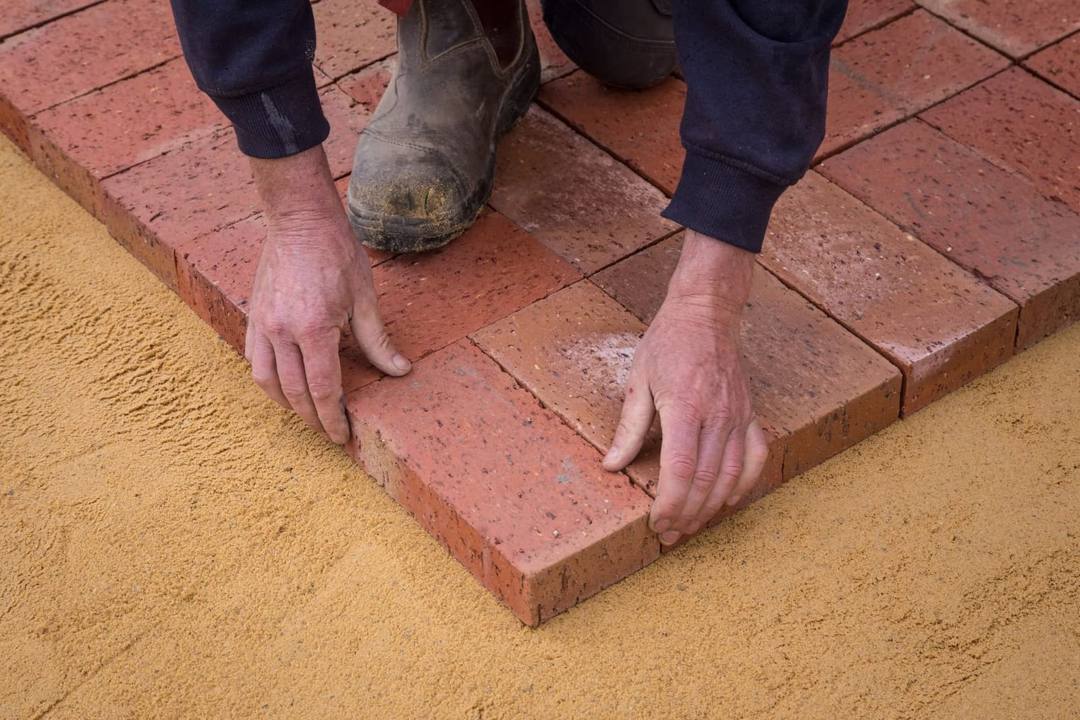 Installer setting clay brick pavers on a screeded sand bedding layer