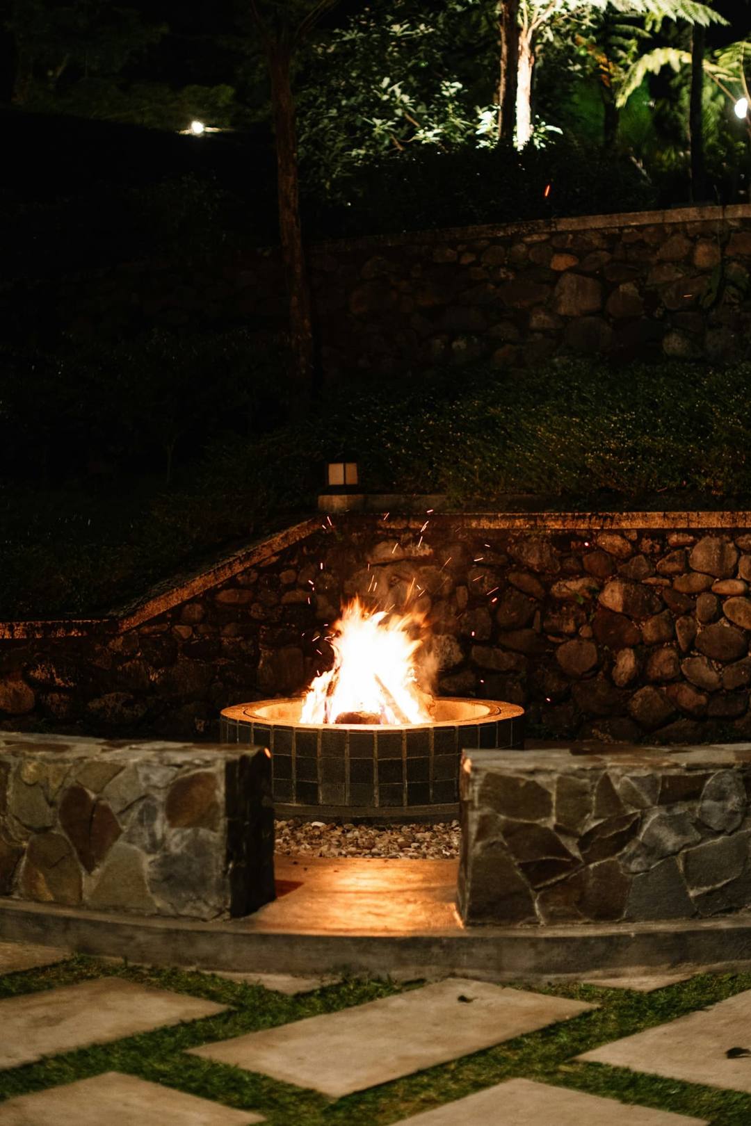 Fire pit blazing in front of a natural stone wall at night